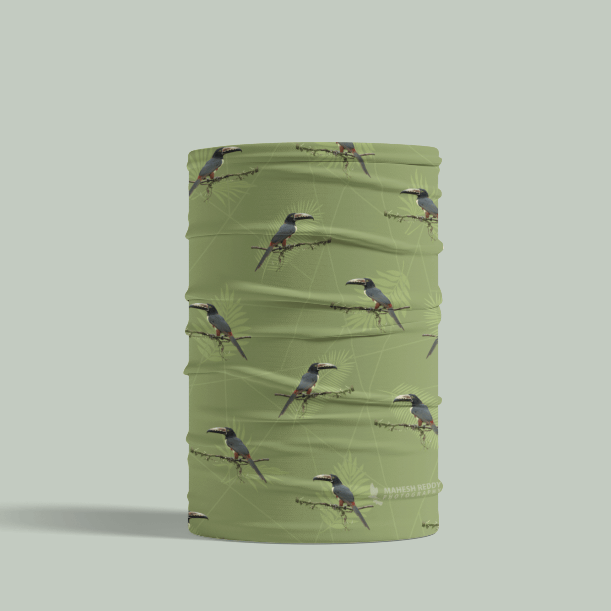 Green Tucktribe neck gaiter with collared aracari bird pattern on a light gray background