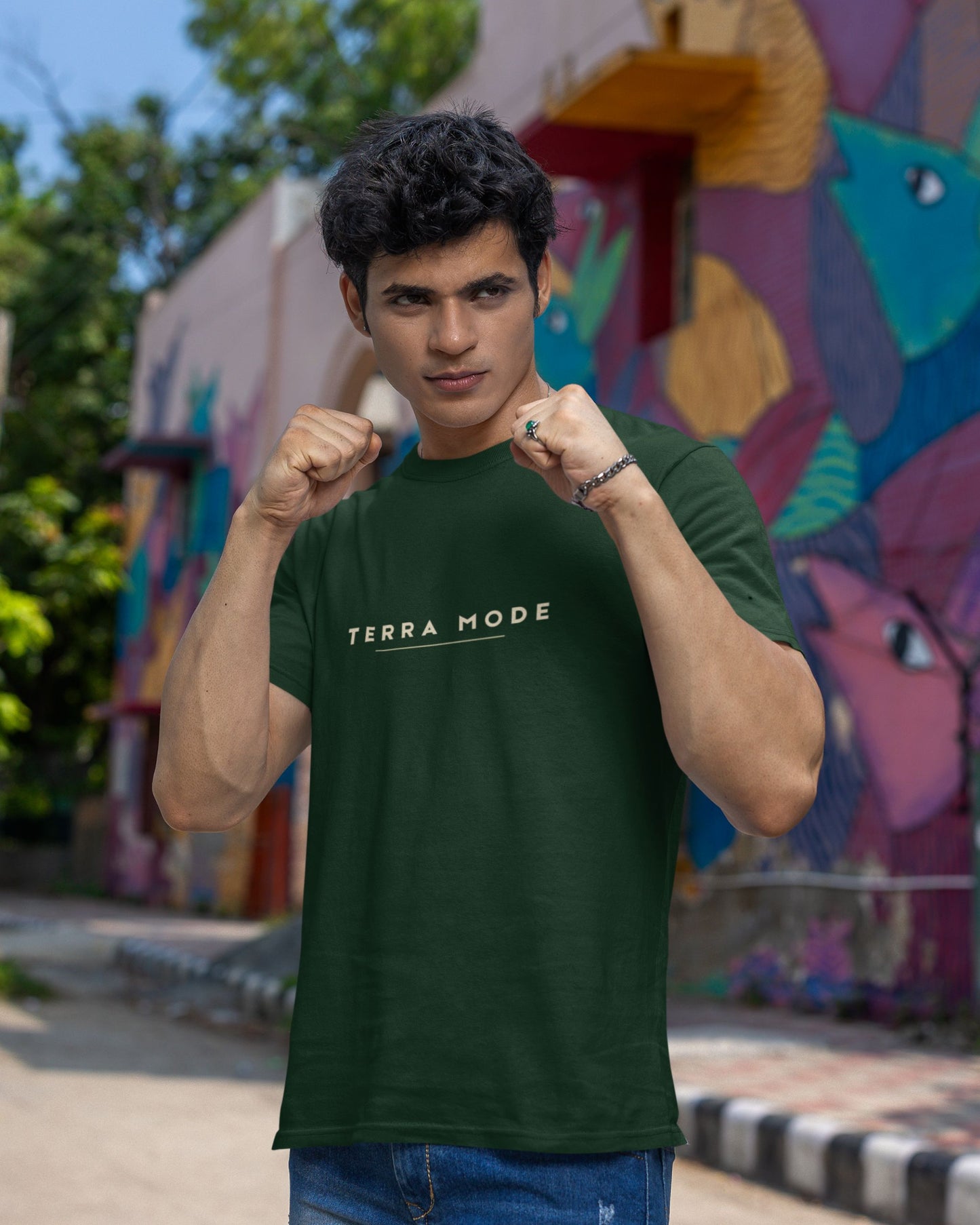 Person wearing a Tucktribe green 'Terra Mode' t-shirt in front of a colorful mural.