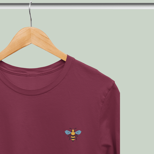 Maroon tucktribe t-shirt with a bee design on a wooden hanger against a light green background