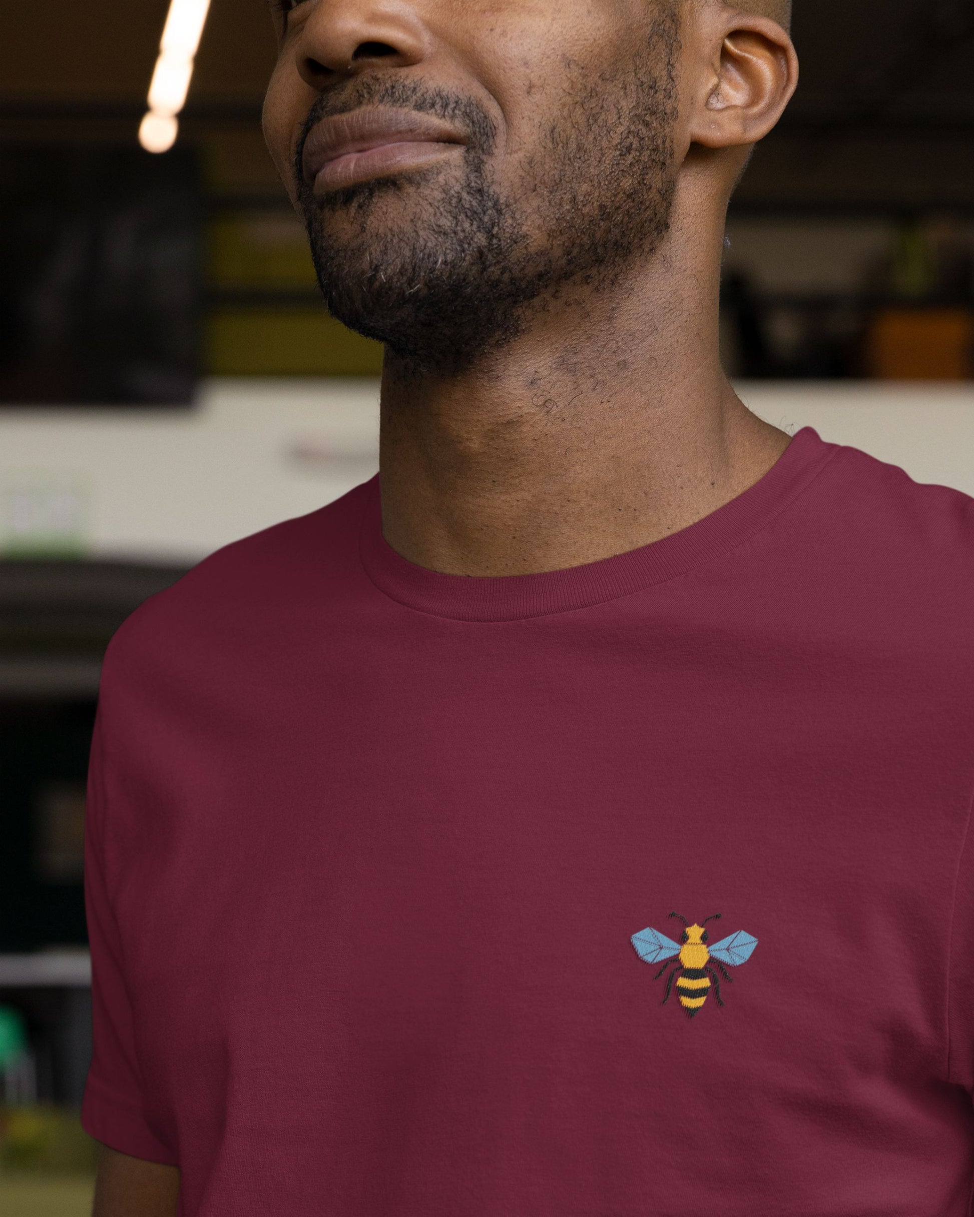 Man wearing a maroon tucktribe t-shirt with a bee design on a blurred background
