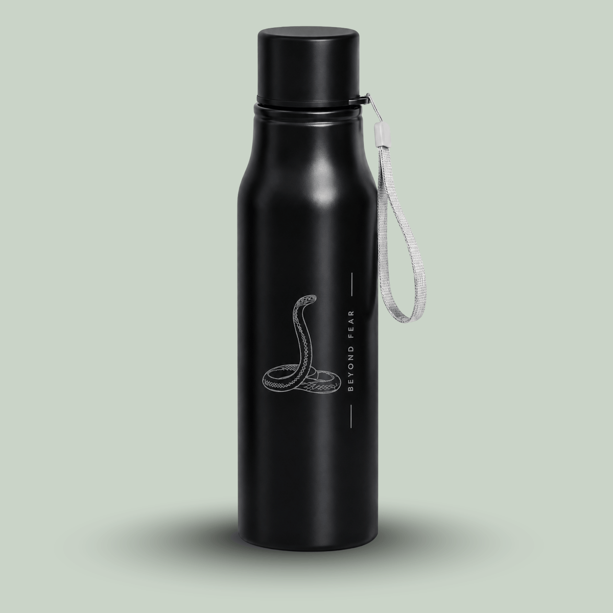 A matte black insulated tucktribe water bottle with a matching black screw cap and a white wrist strap, featuring a engraving of a cobra and the text 'BEYOND FEAR' on the front, set against a solid pale sage green background.