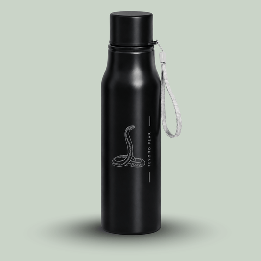 A matte black insulated tucktribe water bottle with a matching black screw cap and a white wrist strap, featuring a engraving of a cobra and the text 'BEYOND FEAR' on the front, set against a solid pale sage green background.
