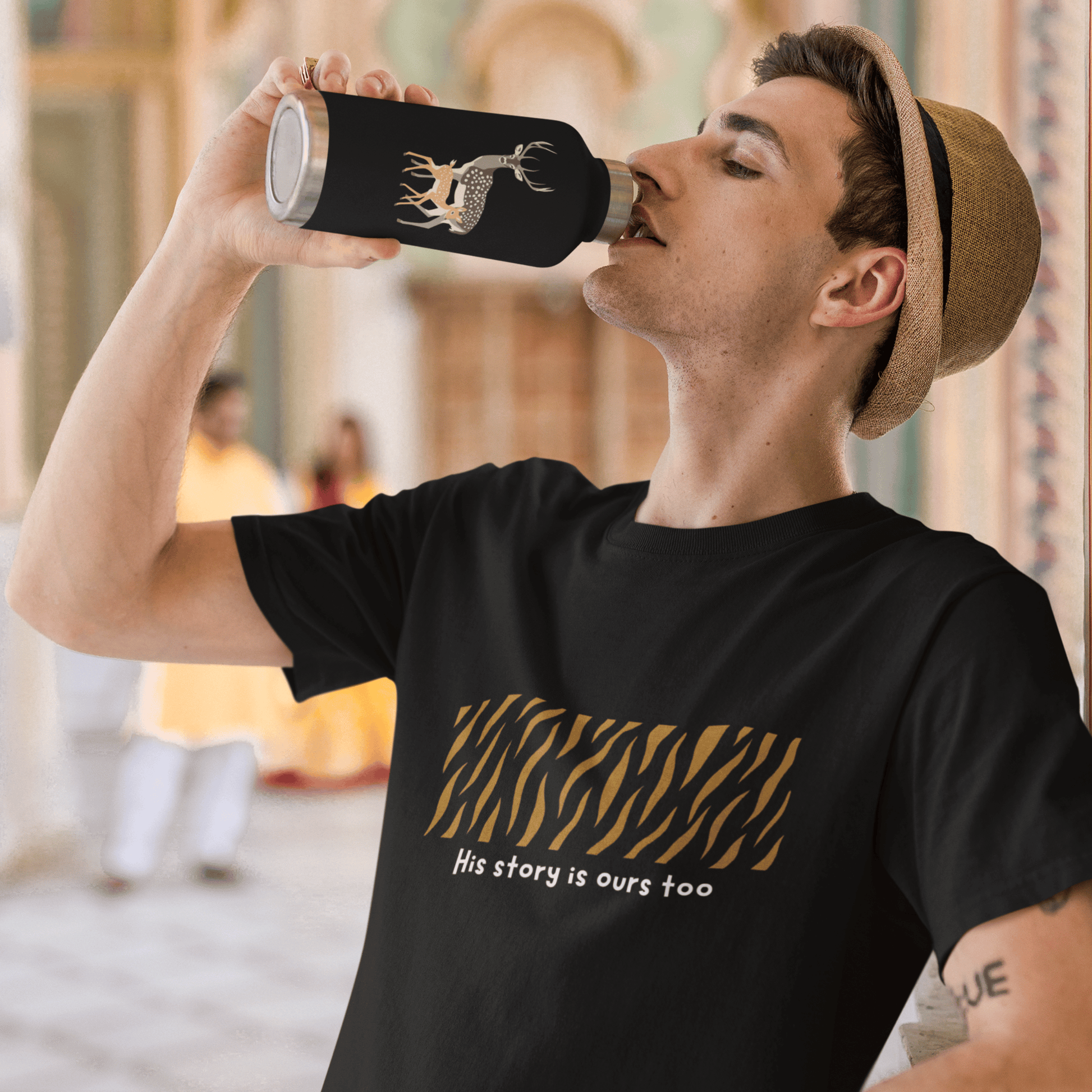 Man drinking from a black water bottle with a design, wearing a black t-shirt with text and graphics.