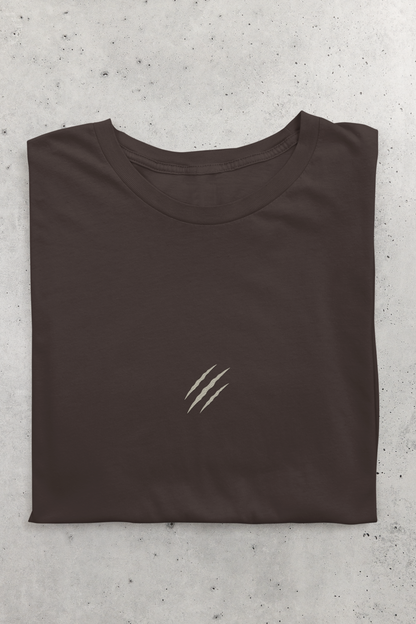 Folded tucktribe brown t-shirt with a small claw scratch embroidery on a gray concrete surface
