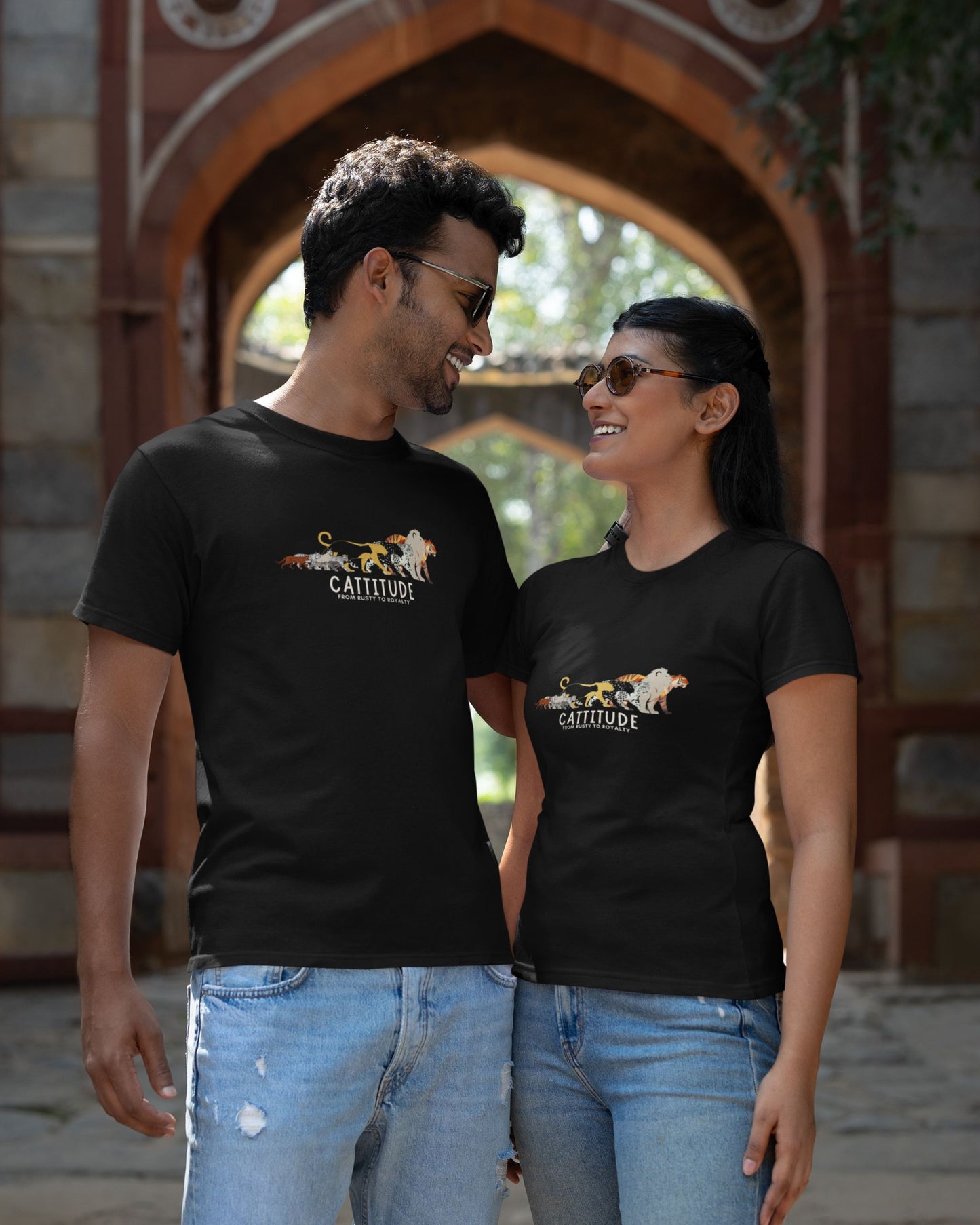 Two people wearing matching tucktribe black t-shirts with a wild cats graphics and cattitude text, standing in front of an archway.