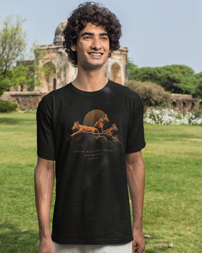 Man wearing a black Dhole wildlife T-shirt featuring three Indian wild dogs on a rocky landscape with sunset-inspired artwork