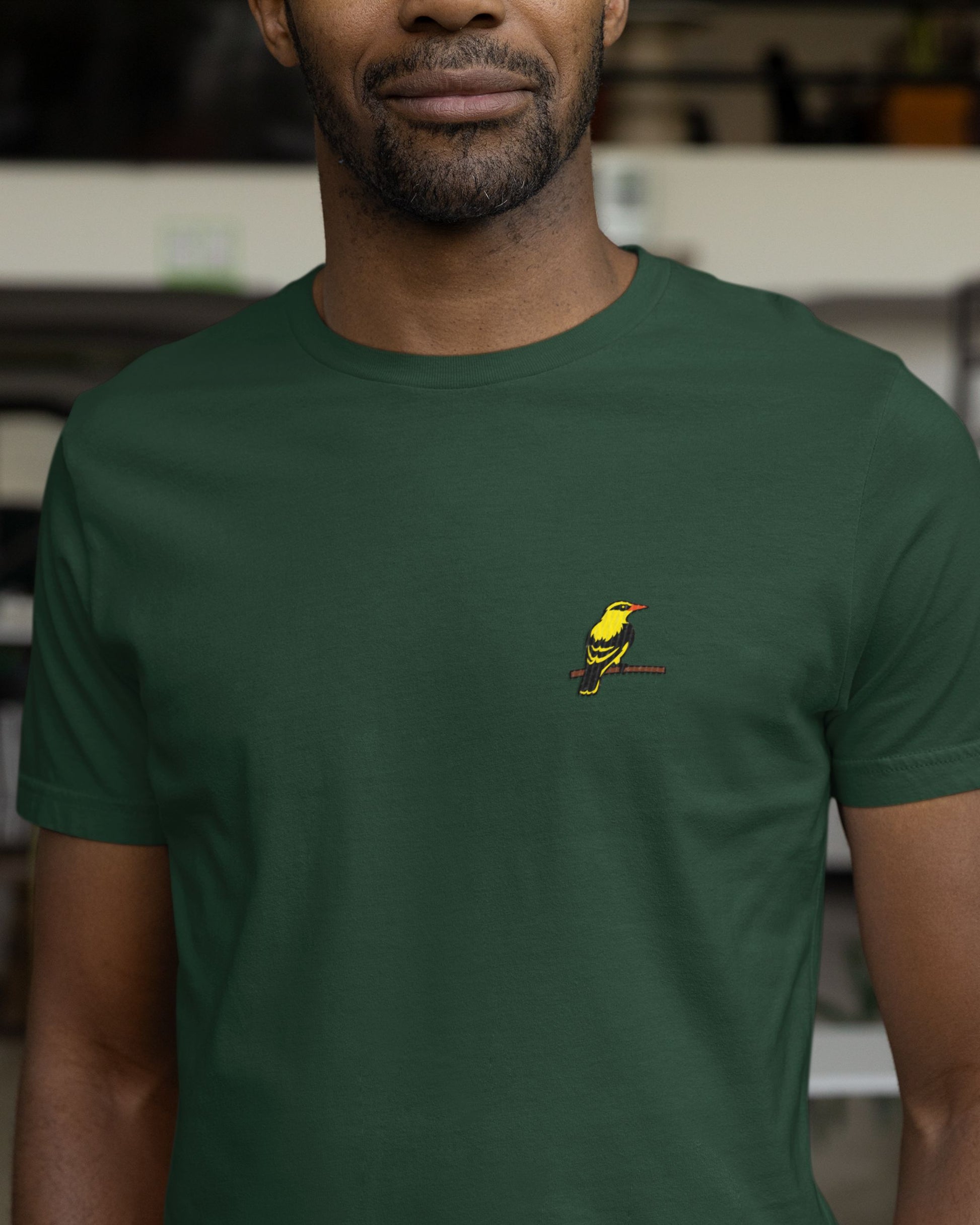 Person wearing a green tucktribe t-shirt with a small embroidery of a golden oriole on  the chest.