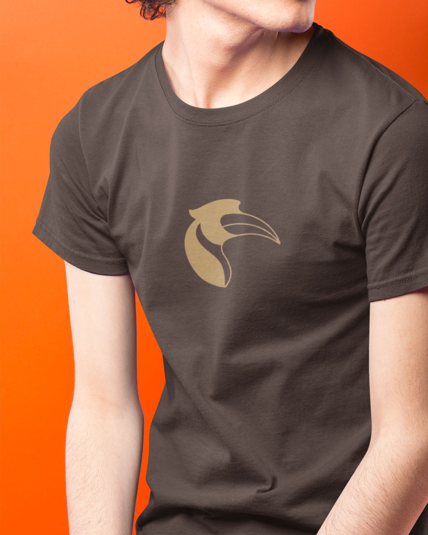 Person wearing a dark brown tucktribe t-shirt with a gold hornbill logo on an orange background