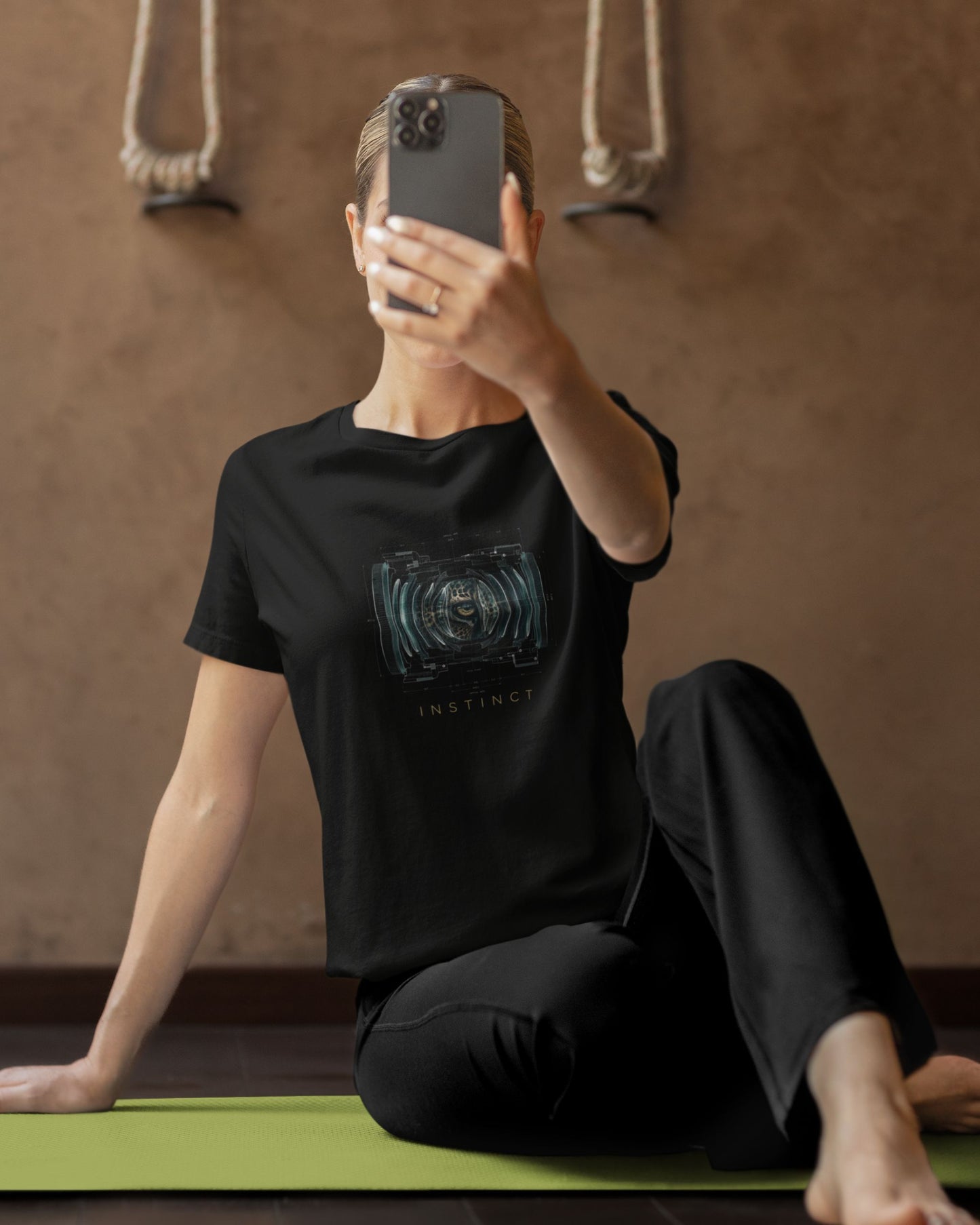 Person taking a mirror selfie wearing a black tucktribe t-shirt with a graphic design on a yoga mat.