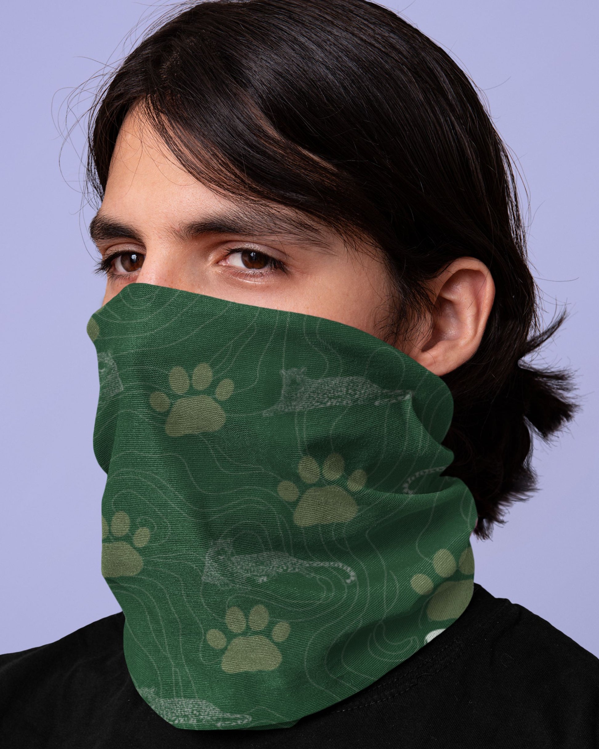Person wearing a Green Tucktribe neck gaiter with leopard paw print pattern  on a light blue background
