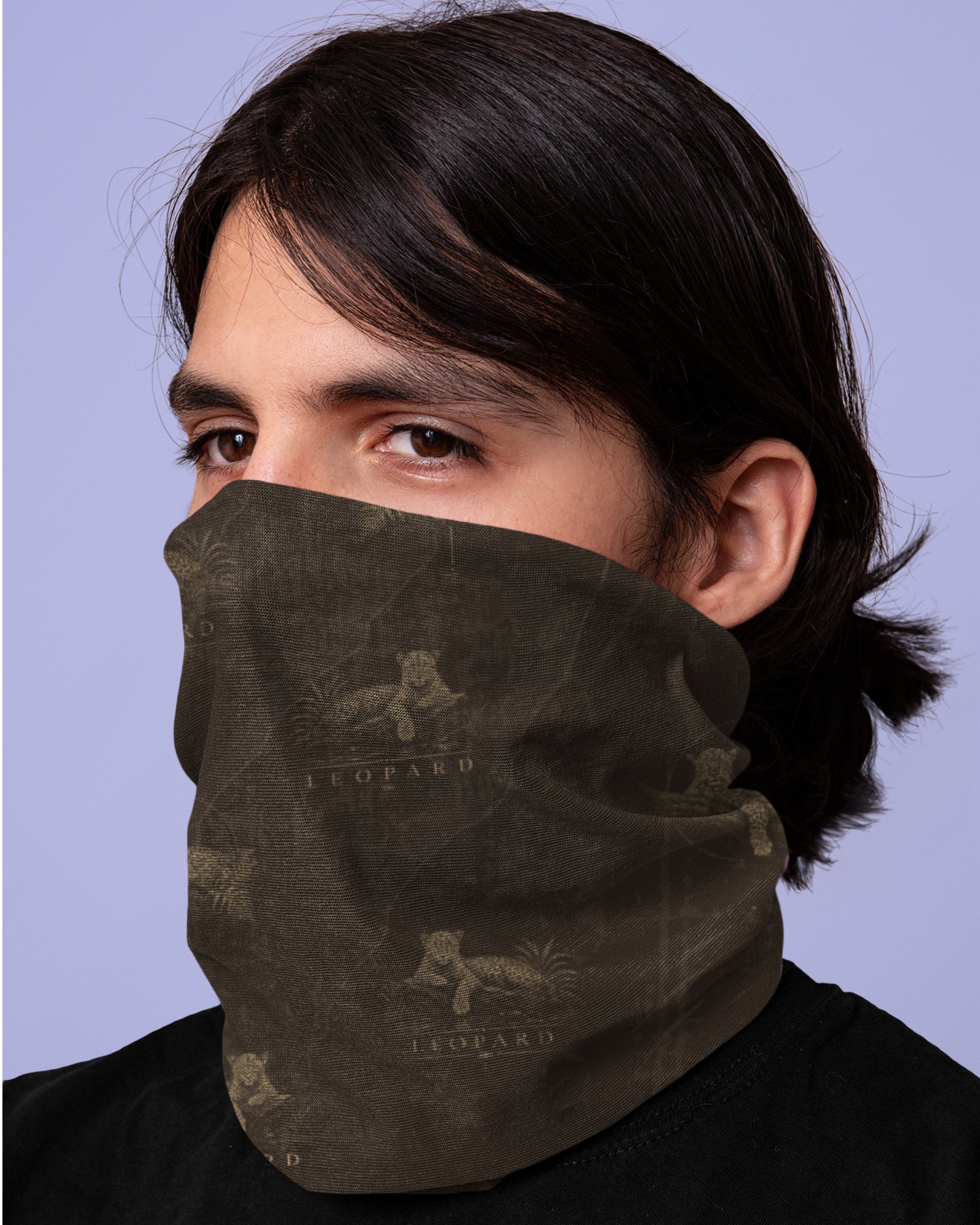 A person wearing a dark brown tucktribe neck gaiter or face covering with a vintage leopard print pattern, shown against a solid light purple background.