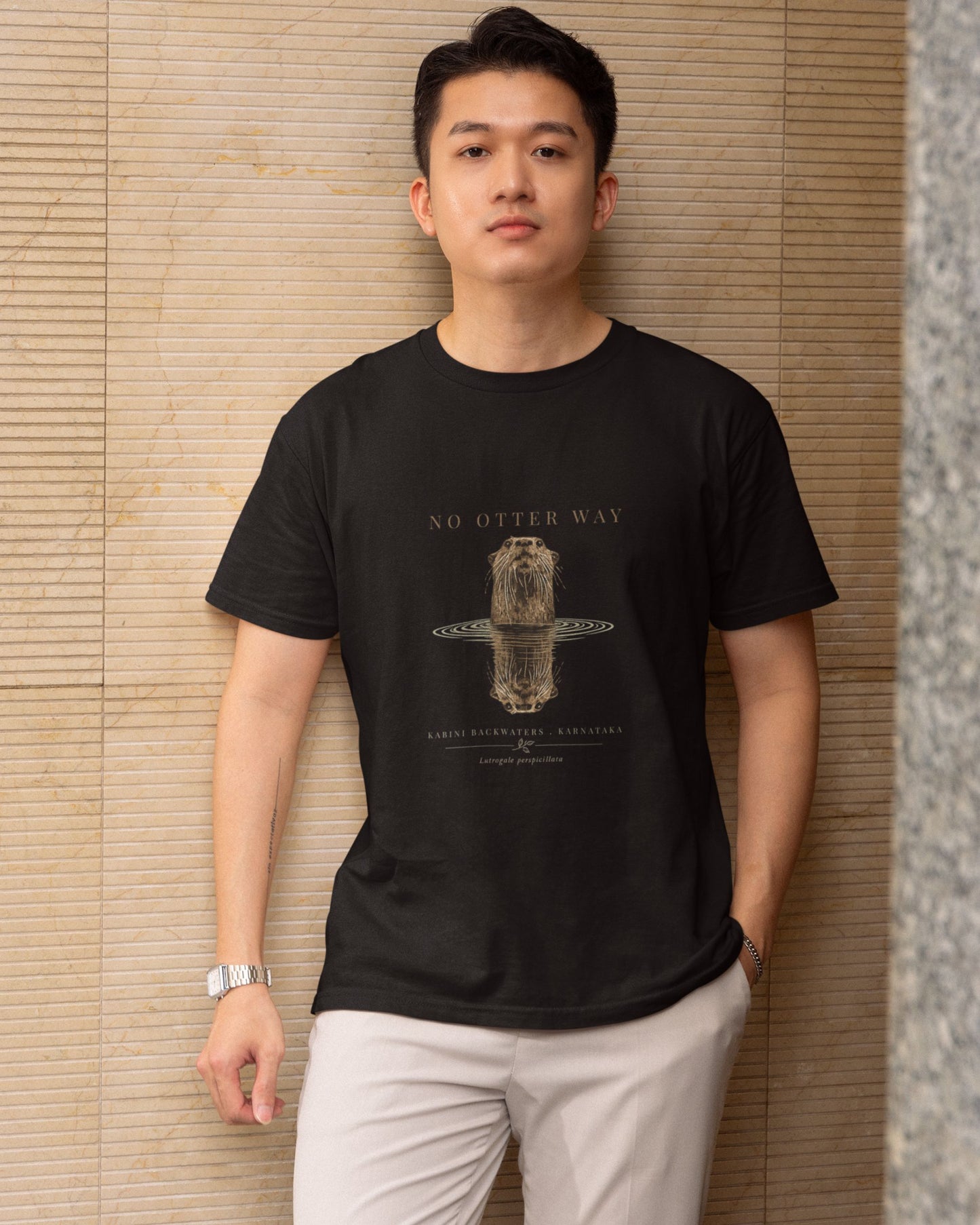 Man wearing a black tucktribe t-shirt with a otter graphic design against a textured wall.