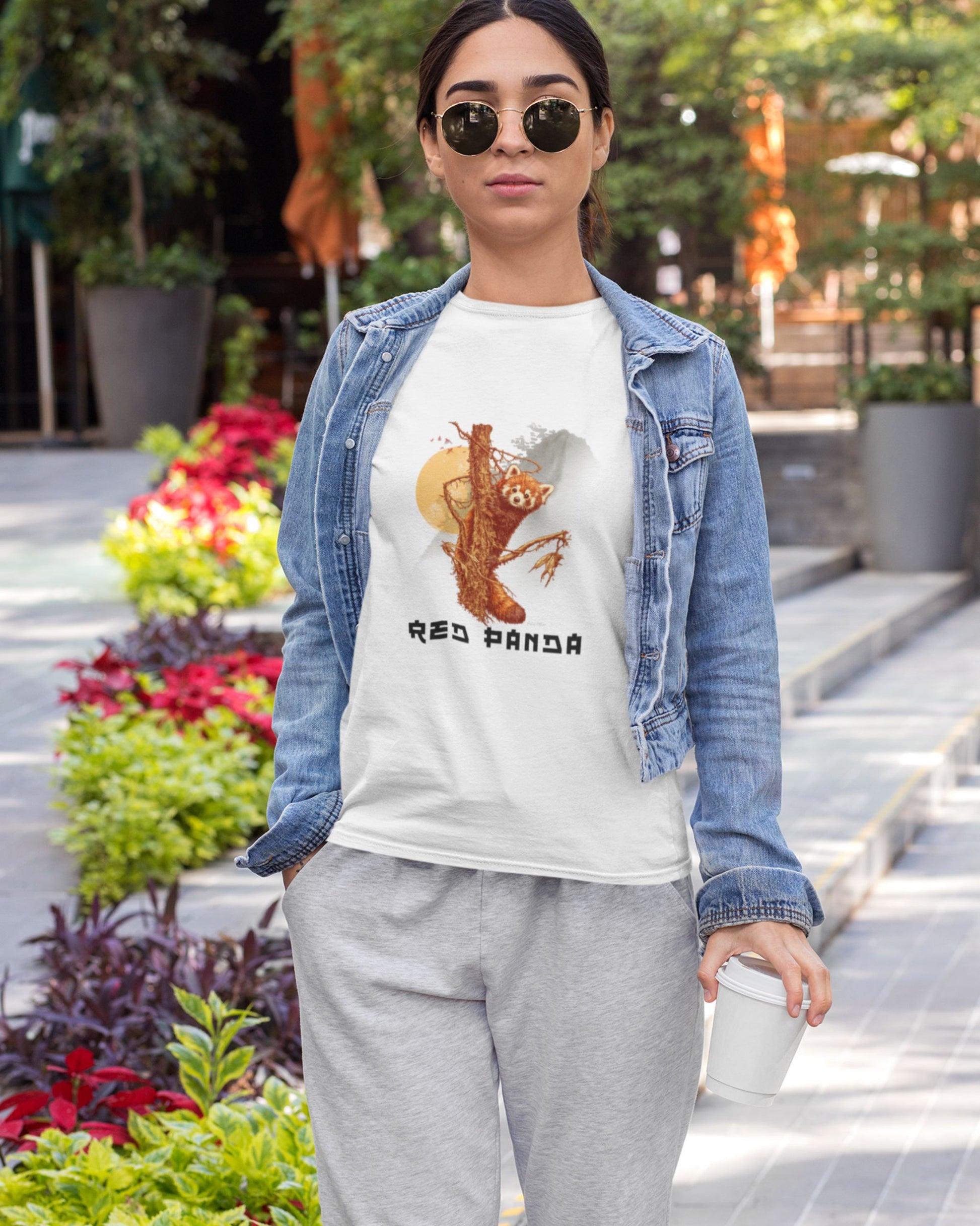 Woman wearing a white tucktribe t-shirt with a red panda graphic and text, standing outdoors.