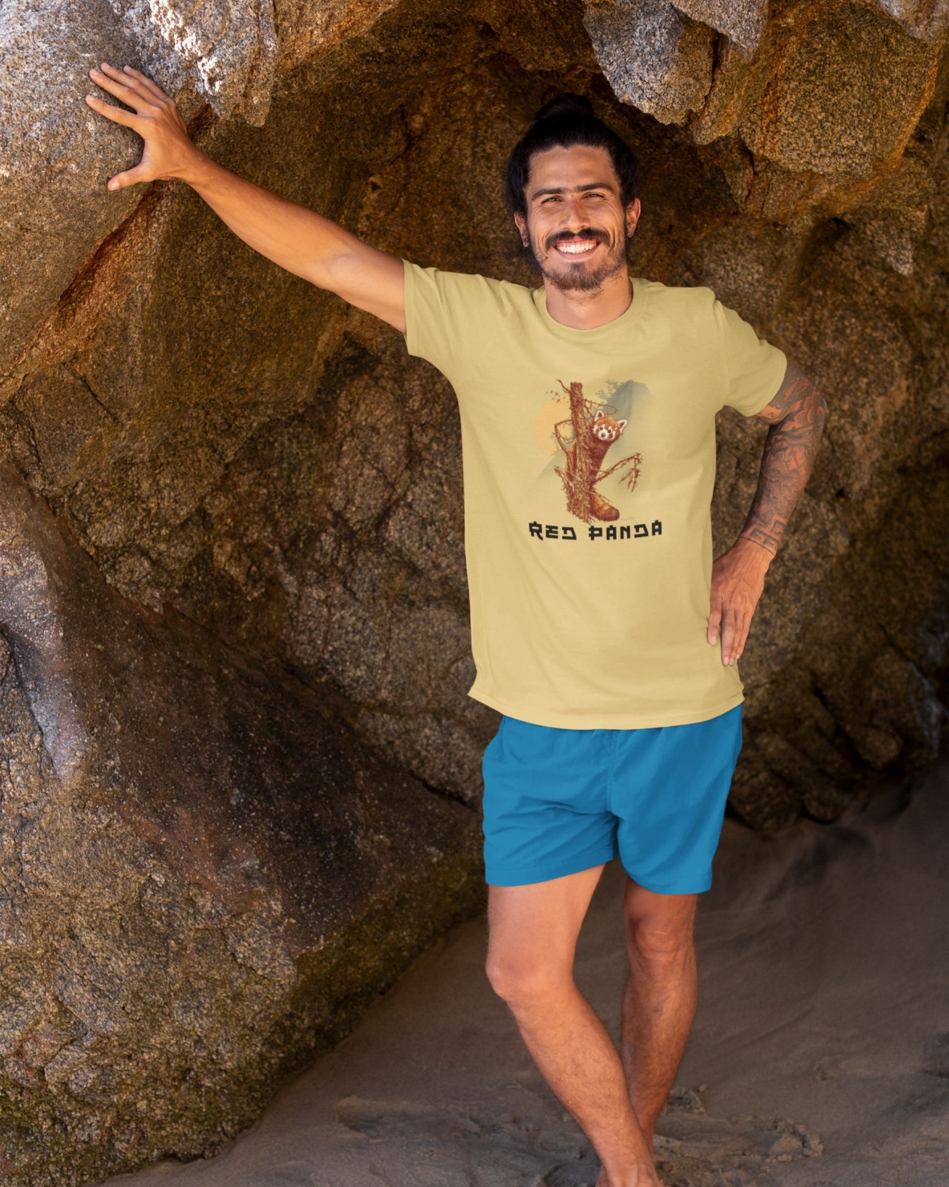Man standing in a cave wearing a beige t-shirt with a graphic design and blue shorts.