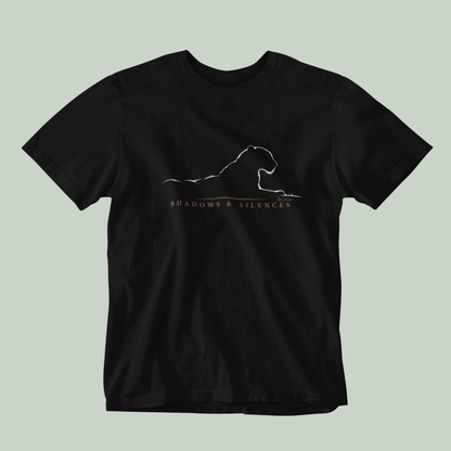 A black short-sleeve crewneck t-shirt featuring a white line art graphic of a leopard from jawai and the text 'SHADOWS & SILENCES' printed on the chest, displayed against a solid light sage green background.