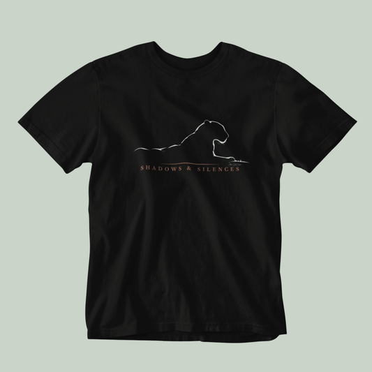 A black short-sleeve crewneck t-shirt featuring a white line art graphic of a leopard from jawai and the text 'SHADOWS & SILENCES' printed on the chest, displayed against a solid light sage green background.