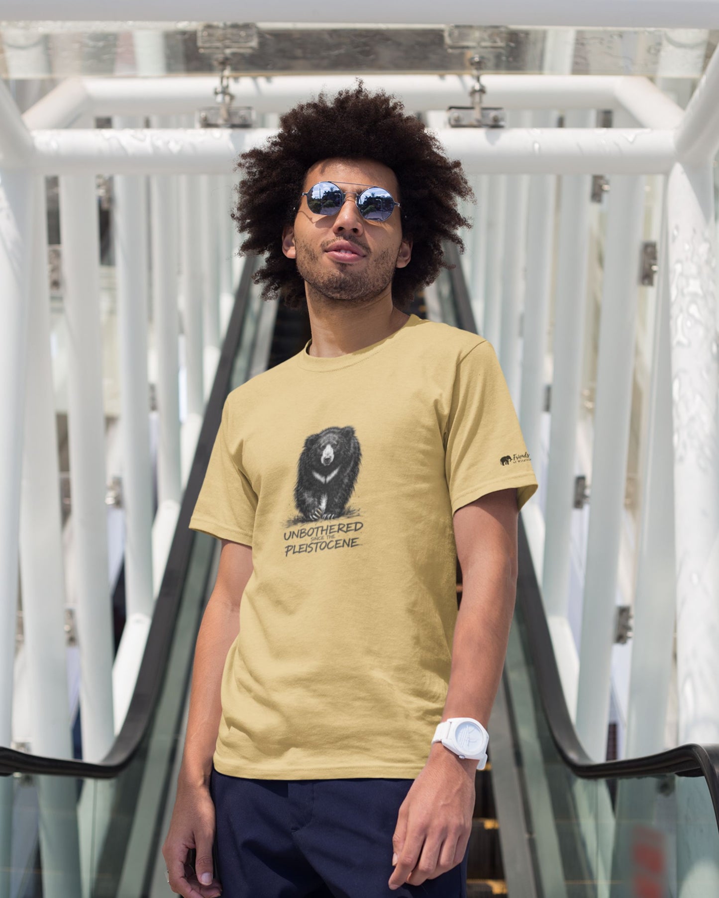 Man wearing a beige t-shirt with a graphic design, standing on a modern architectural background.