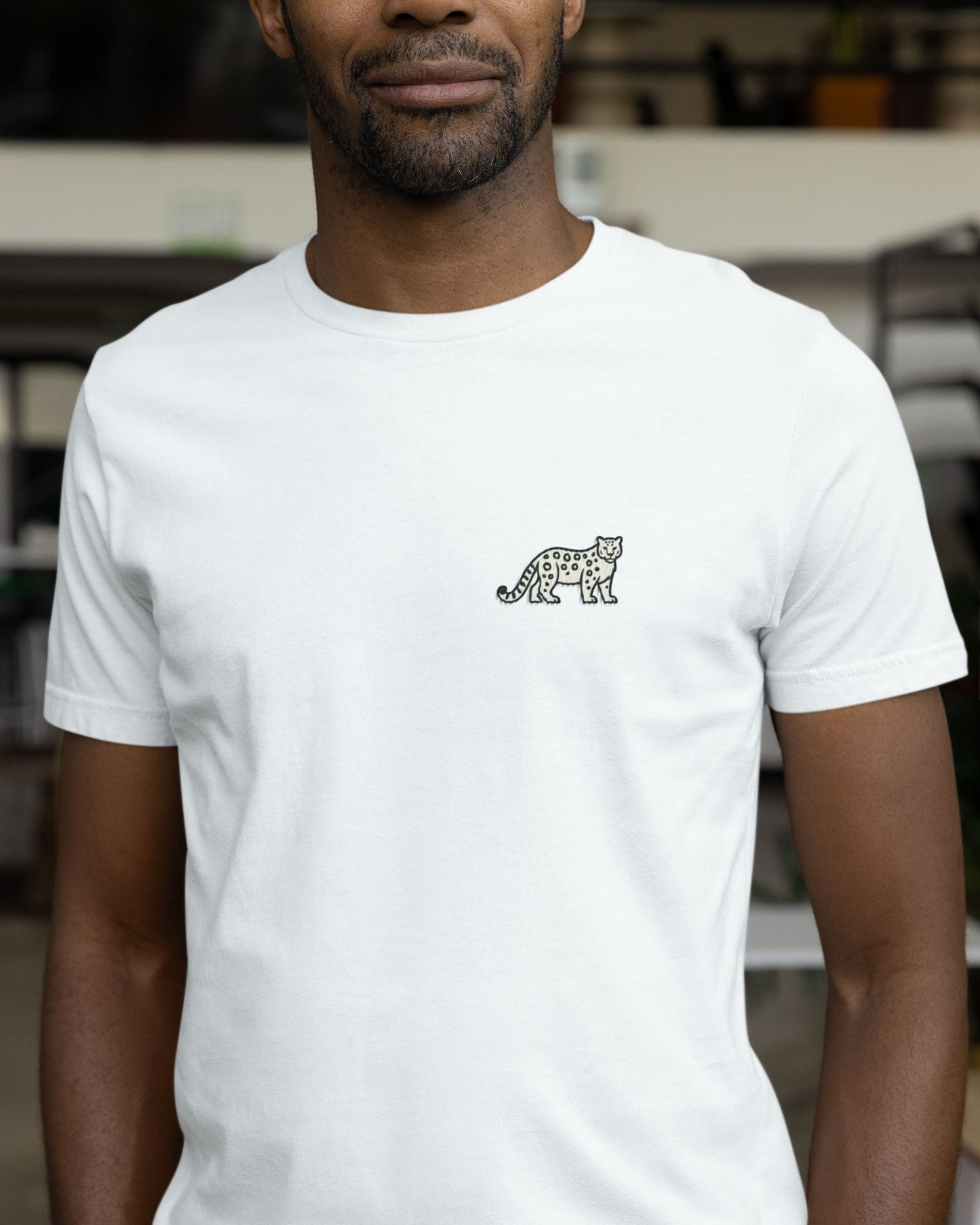 Person wearing white cotton stretch t-shirt with embroidered Snow Leopard wildlife design by Tucktribe