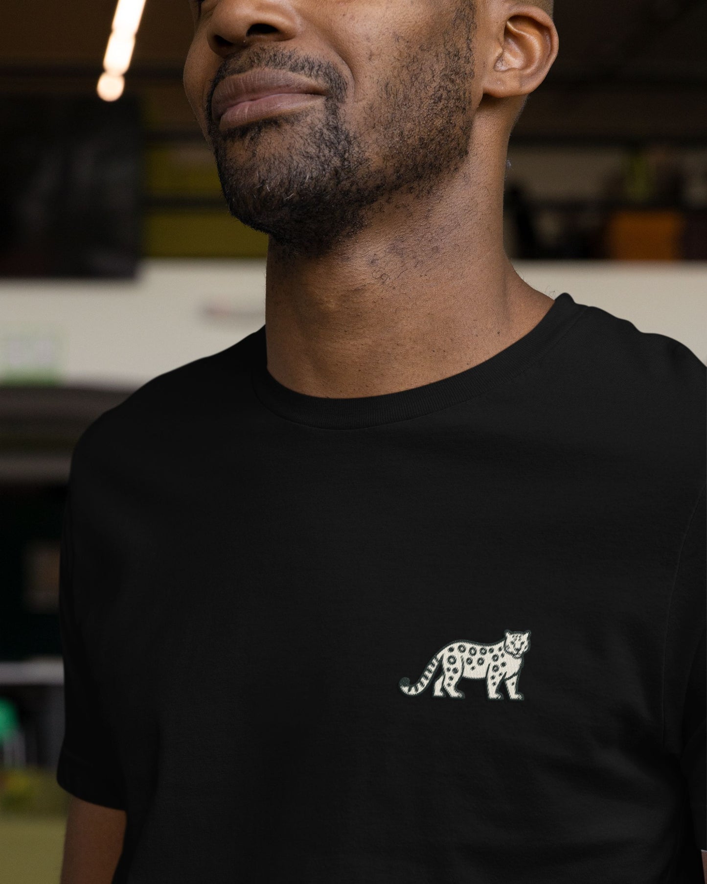Person wearing black cotton stretch t-shirt with embroidered Snow Leopard wildlife design by Tucktribe