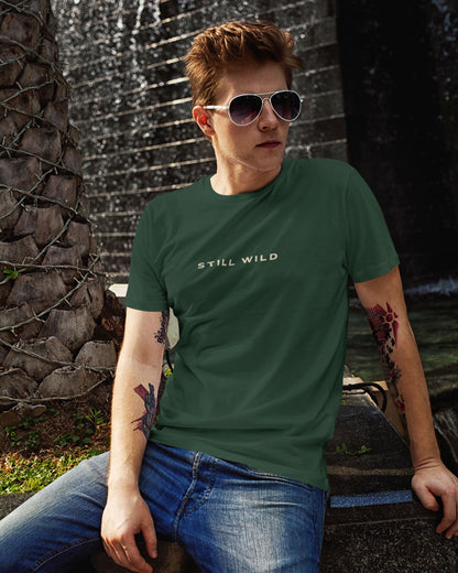 Person wearing a bottle green tucktribe t-shirt with 'STILL WILD' text, sitting outdoors.