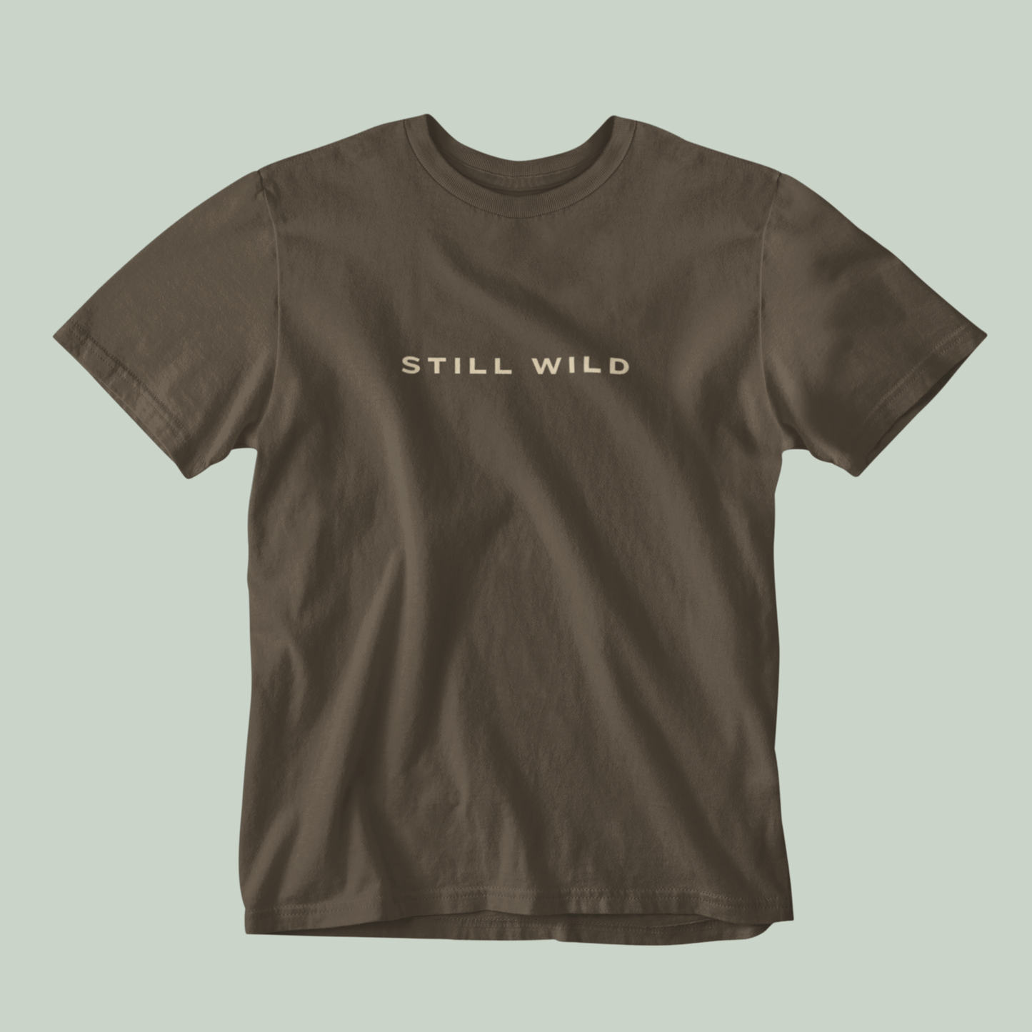Brown tucktribe t-shirt with 'STILL WILD' text on a light green background