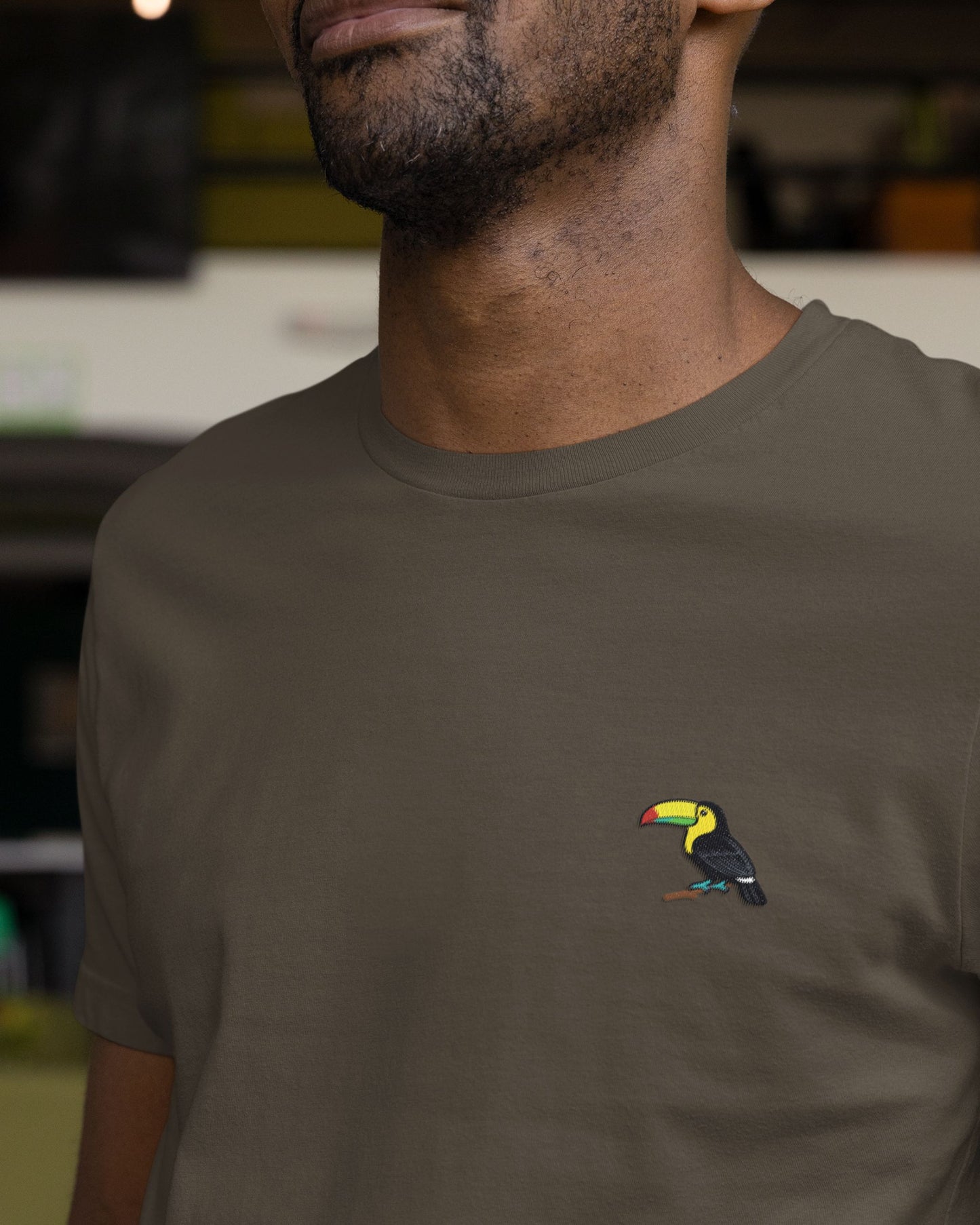 Person wearing a olive green t-shirt with a toucan design on a blurred background