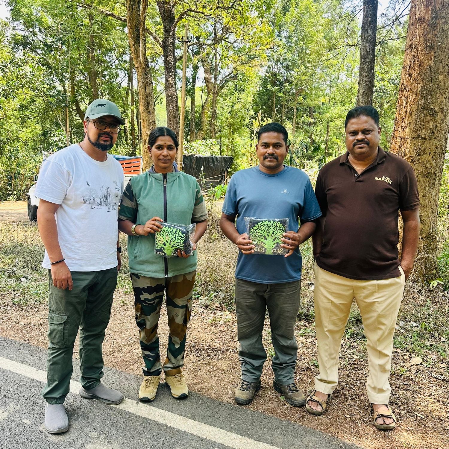Four people standing outdoors holding prints of a tree, with a forest background.