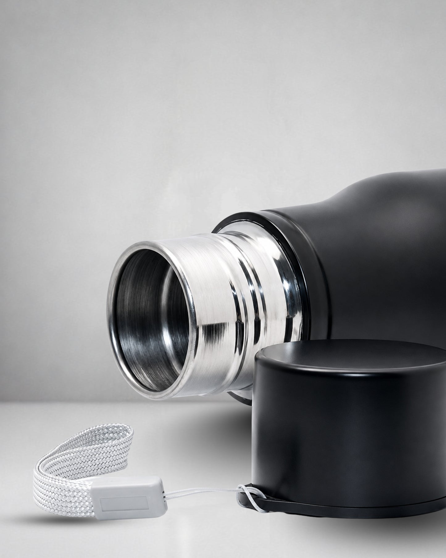 closeup of a matte black insulated tucktribe water bottle with a matching black screw cap opend to and a white wrist strap, featuring a engraving of a cobra and the text 'BEYOND FEAR' on the front, set against a warm interior.