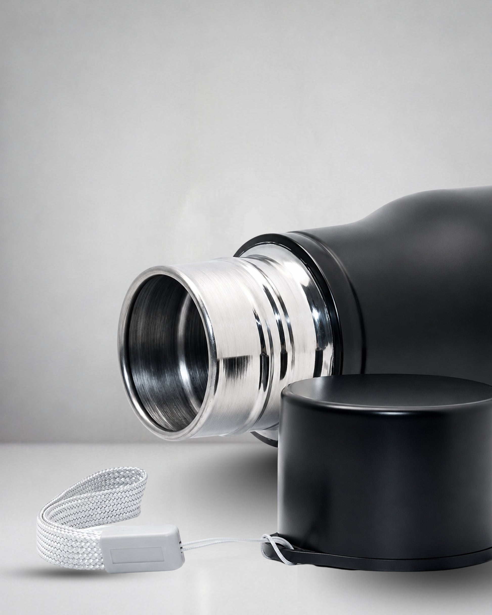 closeup of a matte black insulated tucktribe water bottle with a matching black screw cap opend to and a white wrist strap, featuring a engraving of a cobra and the text 'BEYOND FEAR' on the front, set against a warm interior.